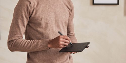 Serious young African-American architect in sweater standing in modern office with pictures on wall and drawing maquette in virtual reality goggles